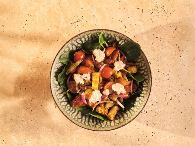 Fotografía de un bowl de ensalada con ingredientes italianos como queso, rúcula, tomate cherry, pollo y deliciosa salsa de pesto original